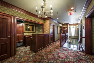 A hallway with patterned carpet, wooden paneling, a chandelier, and an exit sign.
