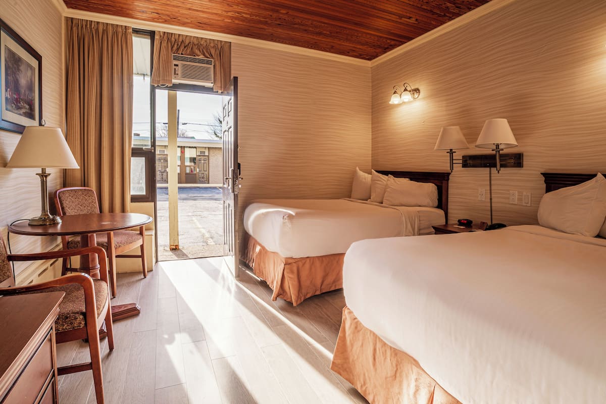 A hotel room with two beds, a desk with a chair, and a small table.