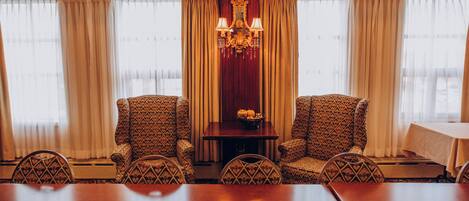 A conference room with a long table, two patterned armchairs, a chandelier, and curtains.