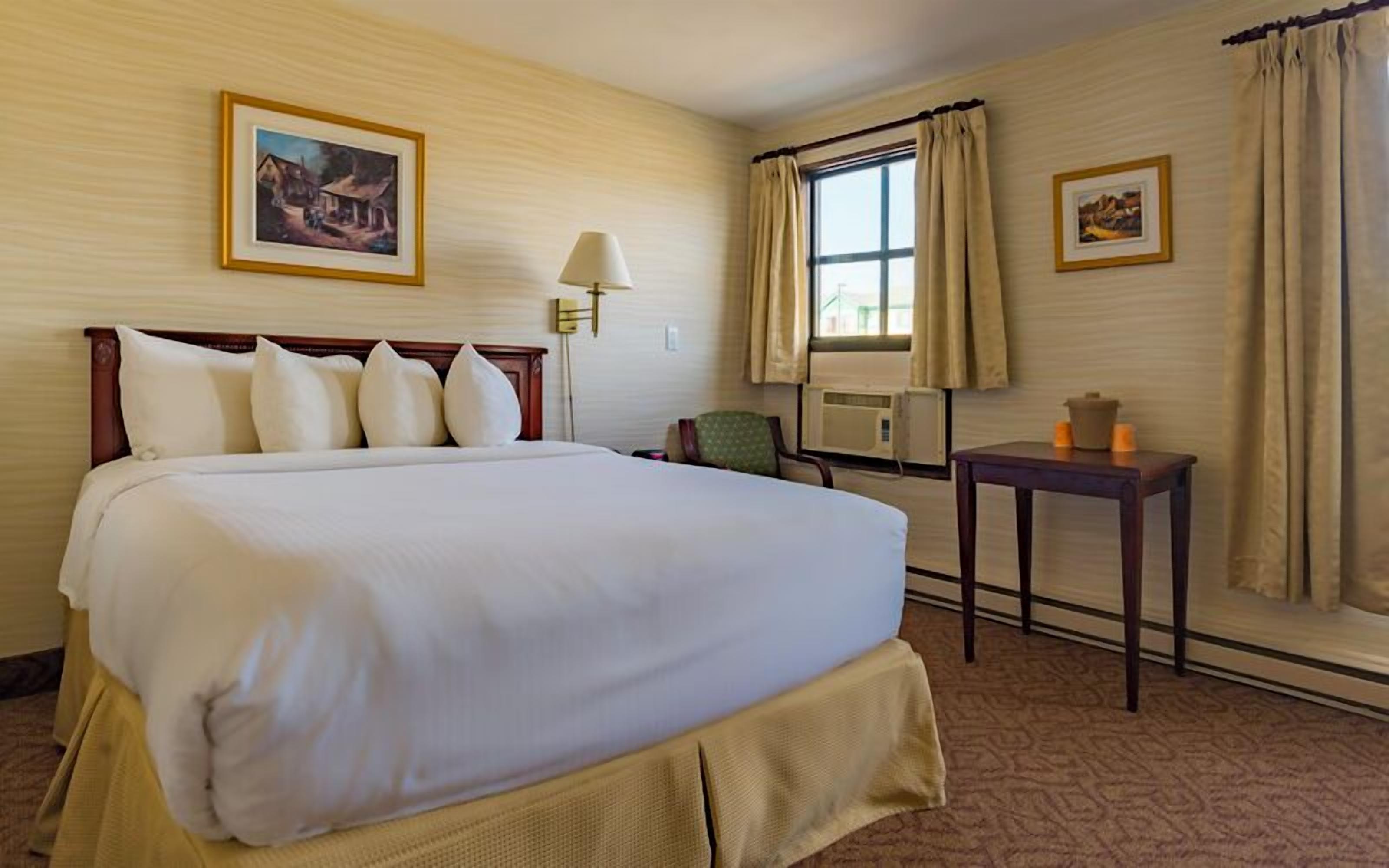 A hotel room with a large bed, a chair, a table with candles, and two framed pictures on the walls.