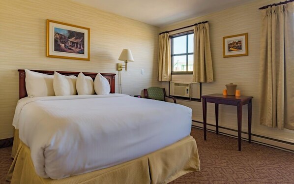 A hotel room with a large bed, a chair, a table with candles, and two framed pictures on the walls.