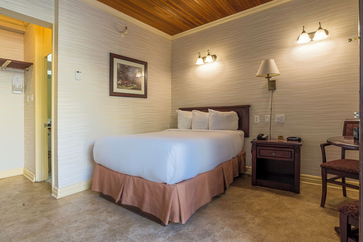 A neatly arranged bedroom with a large bed, bedside table, lamp, and a chair.