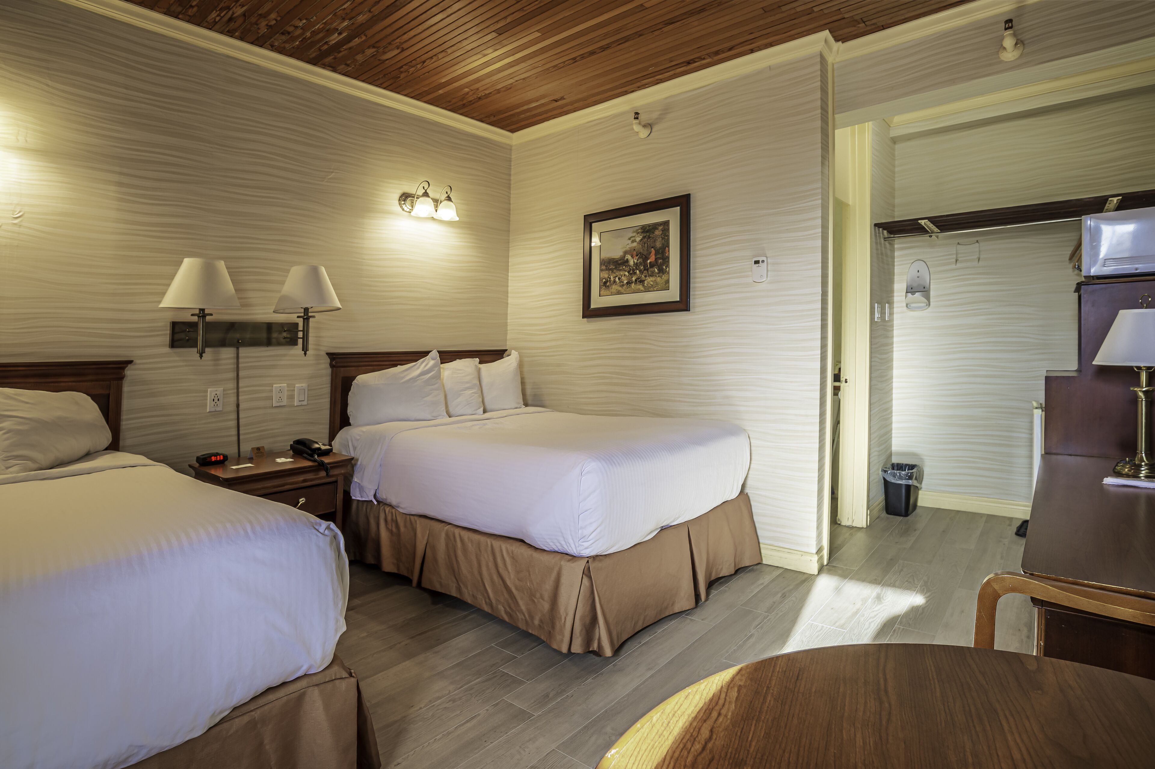 Quarto de hotel com duas camas, uma escrivaninha, uma cadeira e um quadro na parede.