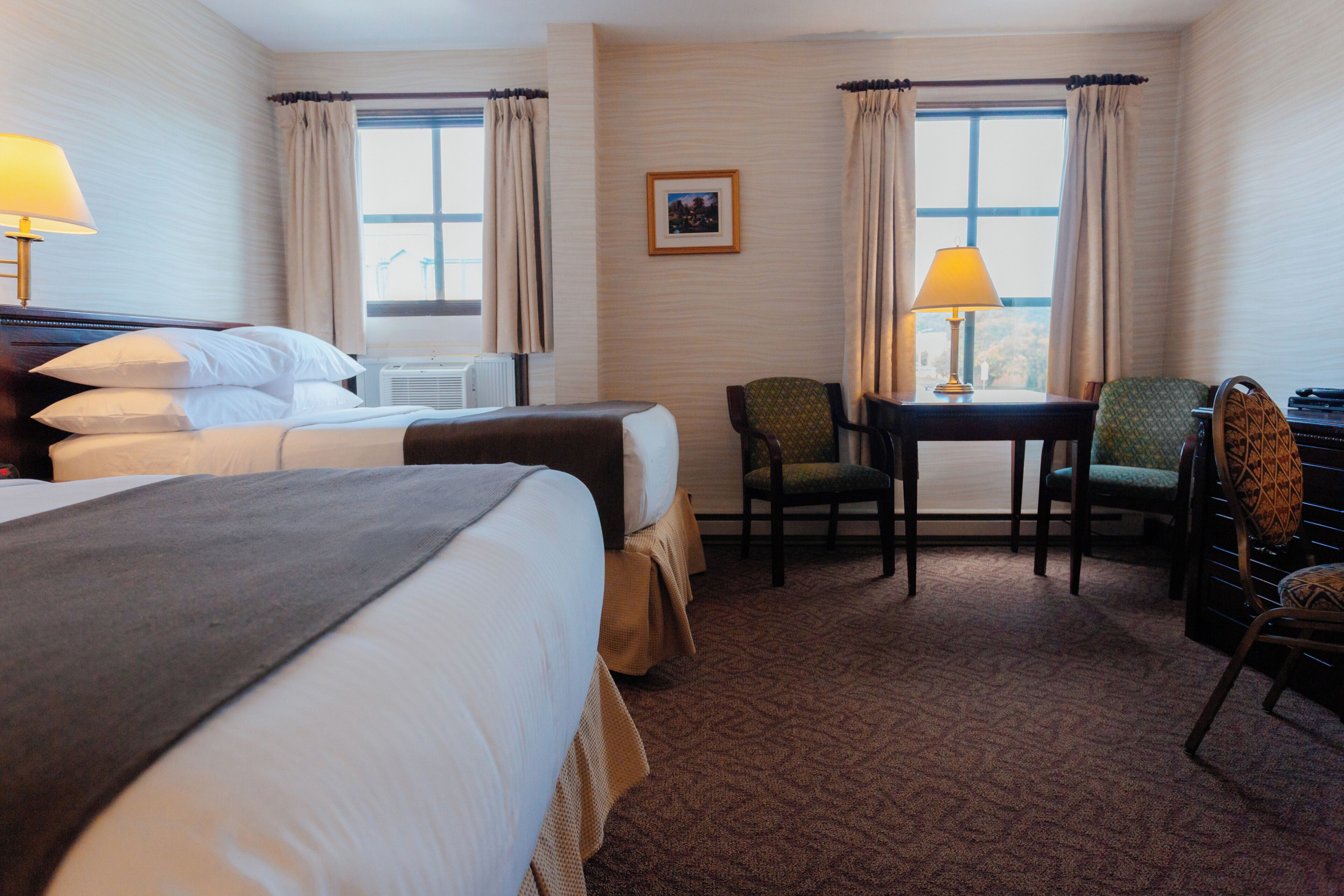 A hotel room with two beds, a desk, a chair, and a window with curtains.