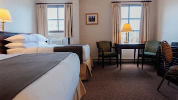 A hotel room with two beds, a desk, a chair, and a window with curtains.