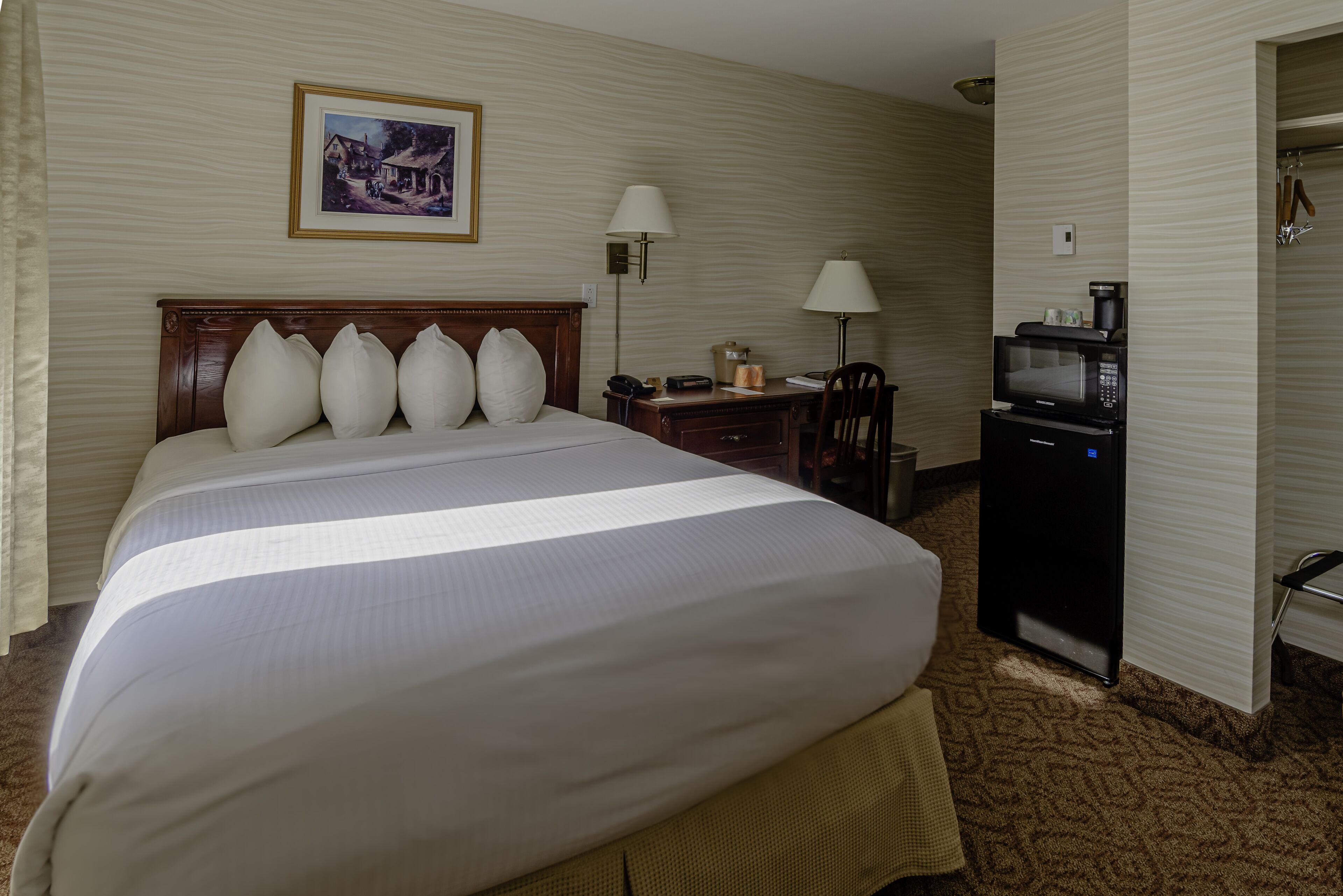 A hotel room with a large bed, a desk with a telephone, a microwave, and a framed picture on the wall.