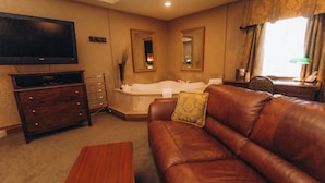 A hotel room with a leather sofa, a flat-screen TV, a bathtub, and a desk with a lamp. - The Guv’nor (St. John's)