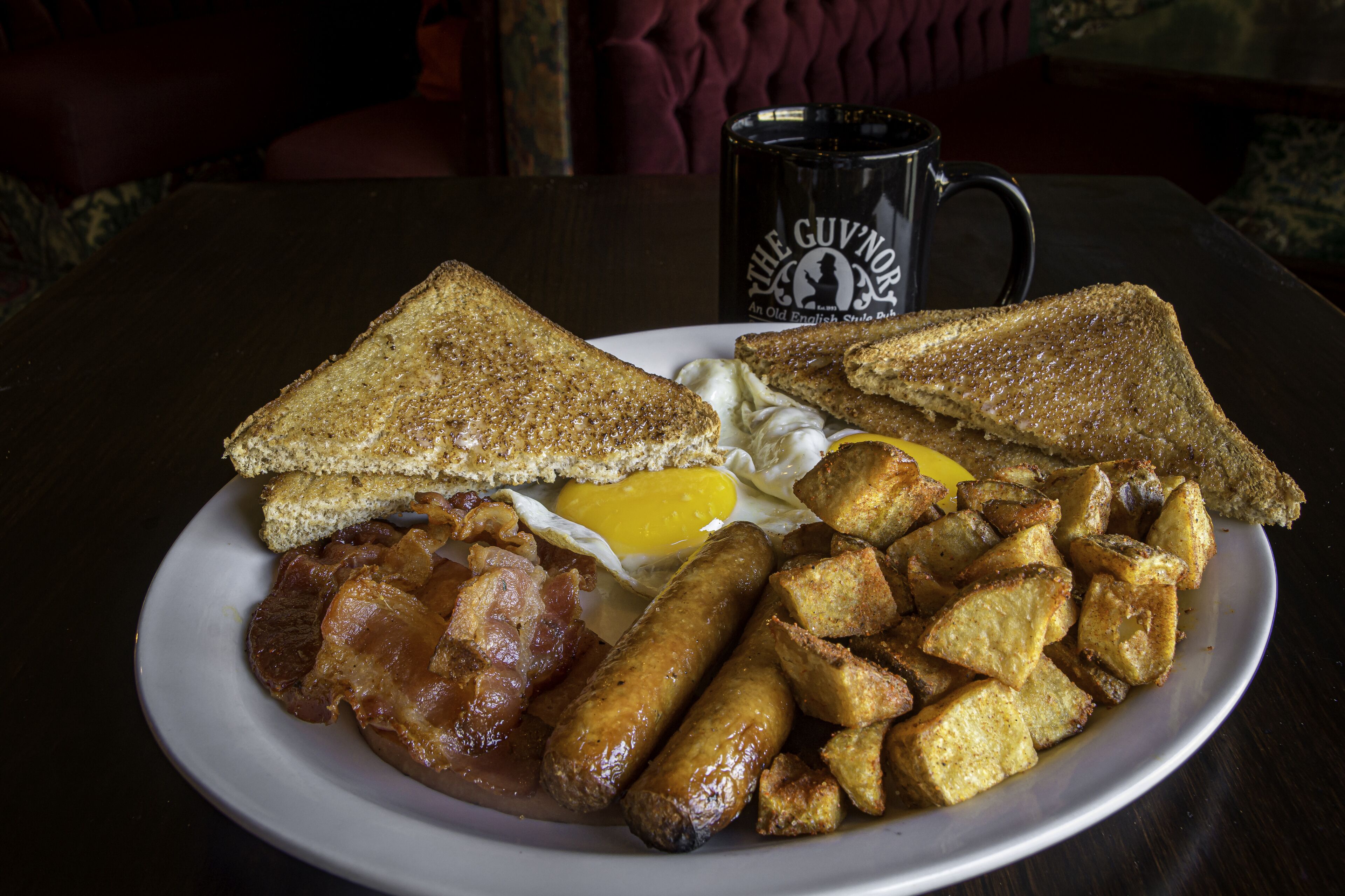 A plate of breakfast food including toast, eggs, bacon, sausages, and fried potatoes.