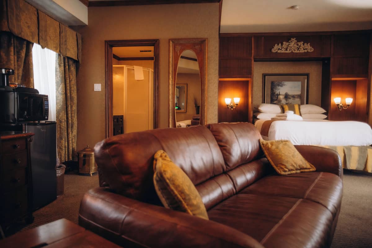 A hotel room with a leather sofa, a bed with white linens, a coffee machine, and wall-mounted sconces.
