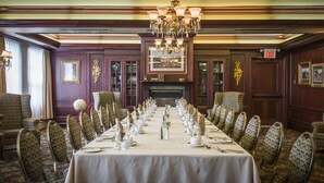 A formal dining room with a long table set for a meal, surrounded by patterned chairs, a chandelier, and framed artwork on the walls. - The Guv’nor (St. John's)