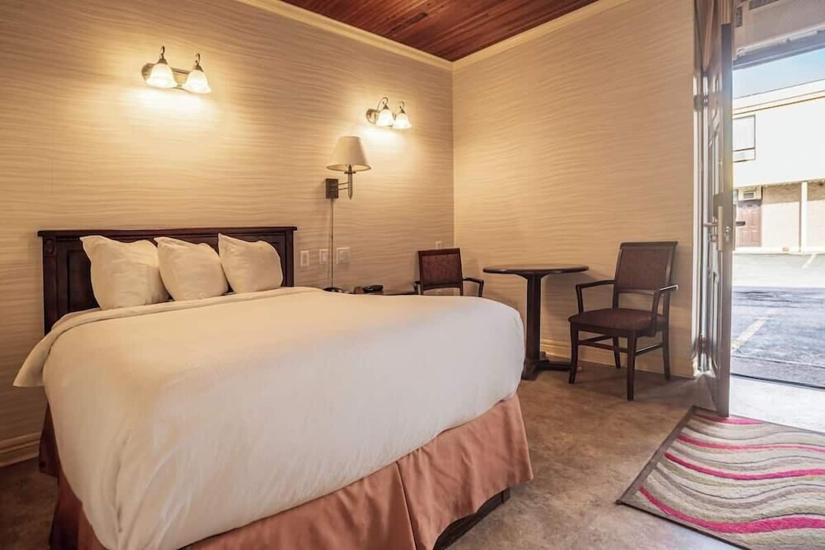 A hotel room with a large bed, a desk, two chairs, and a lamp.