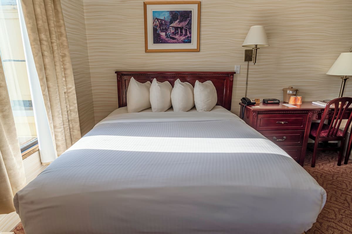 A hotel room with a large bed, a desk with a lamp, a chair, and a painting on the wall.
