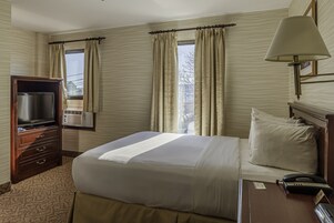 A hotel room with a bed, a TV, a lamp, and a telephone.