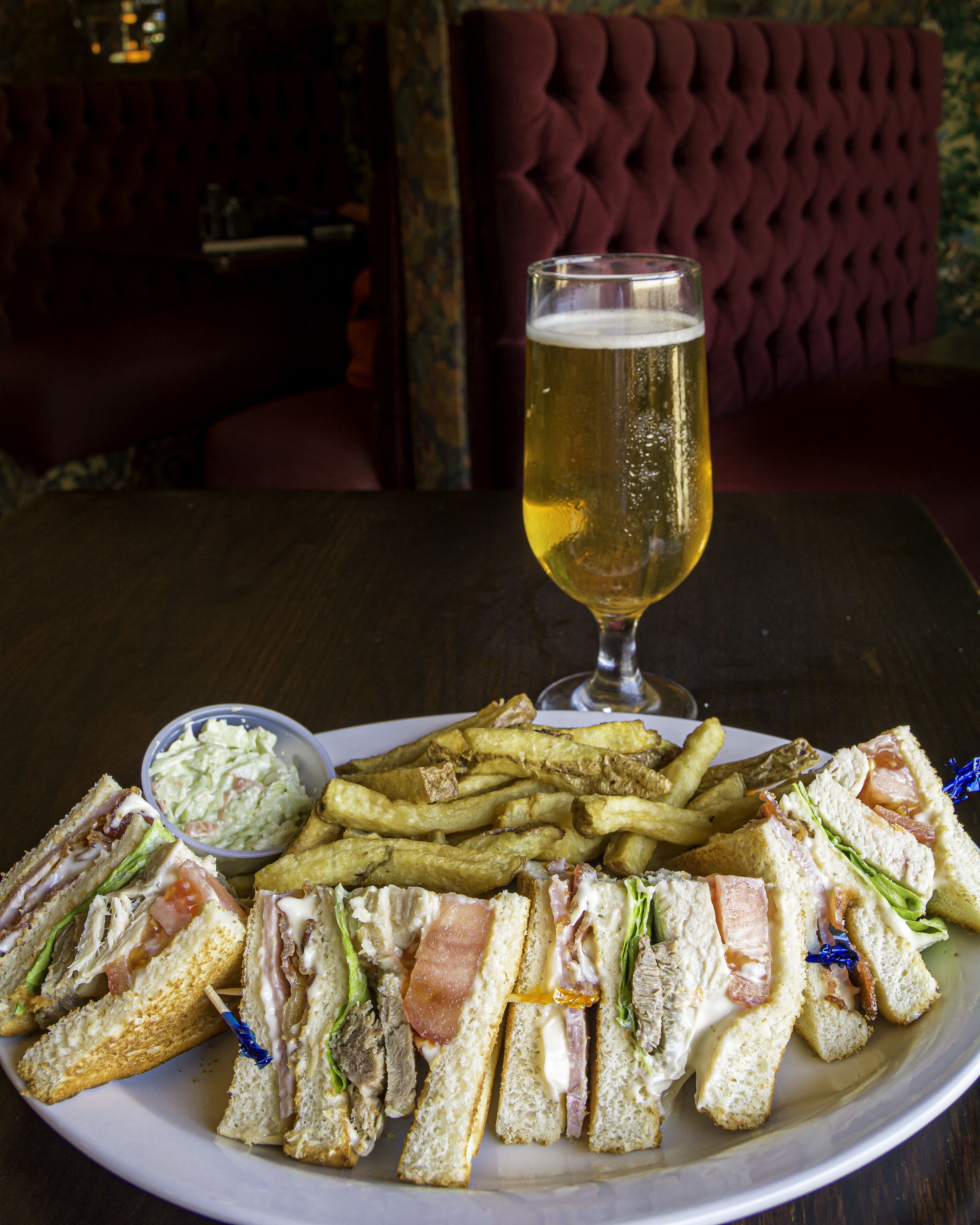 A plate with sandwiches, fries, and a glass of beer on a table.