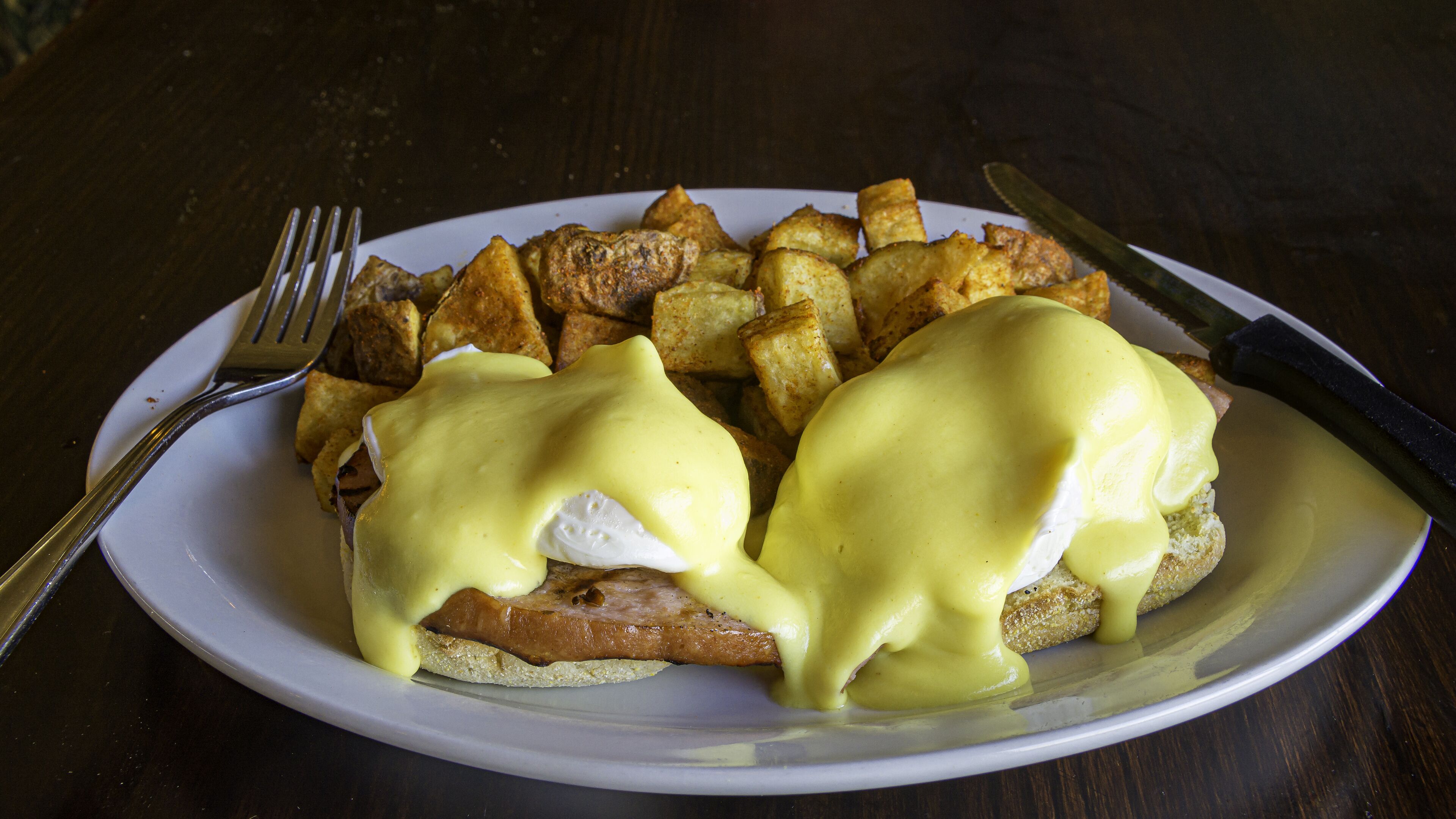 Un plato de huevos benedictinos con hash browns, un cuchillo y un tenedor al lado.