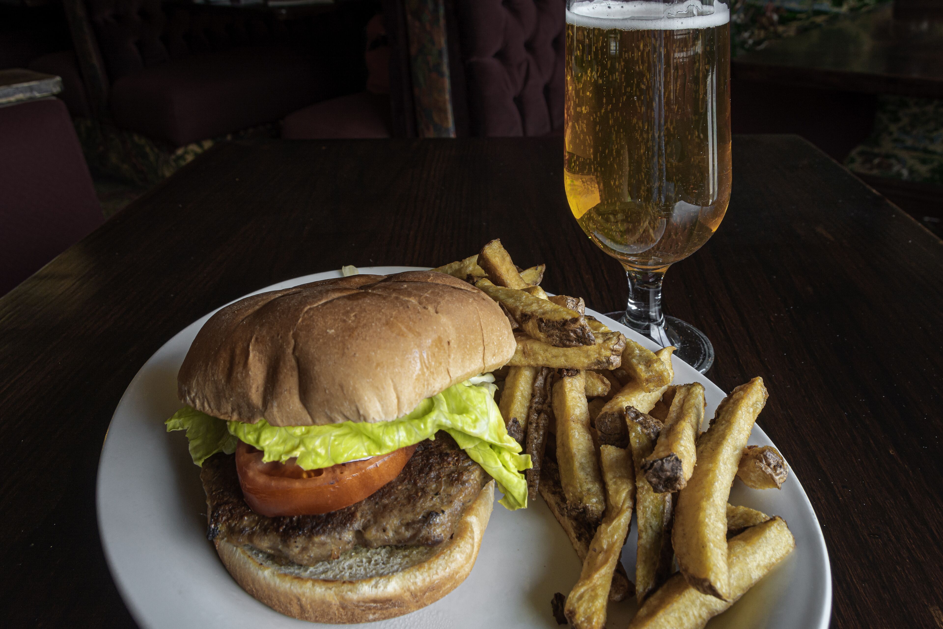 A plate with a burger and fries, and a glass of beer on a table.