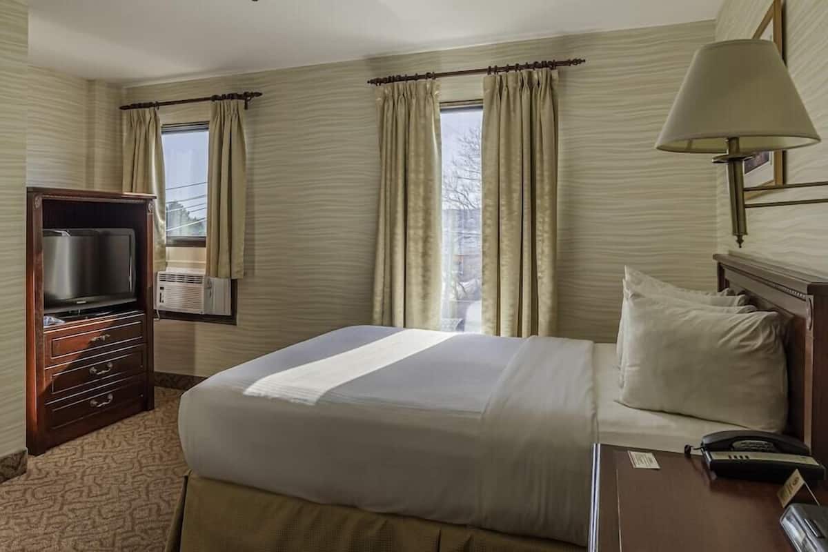 A hotel room with a bed, a TV, a lamp, a phone, and a window with curtains.