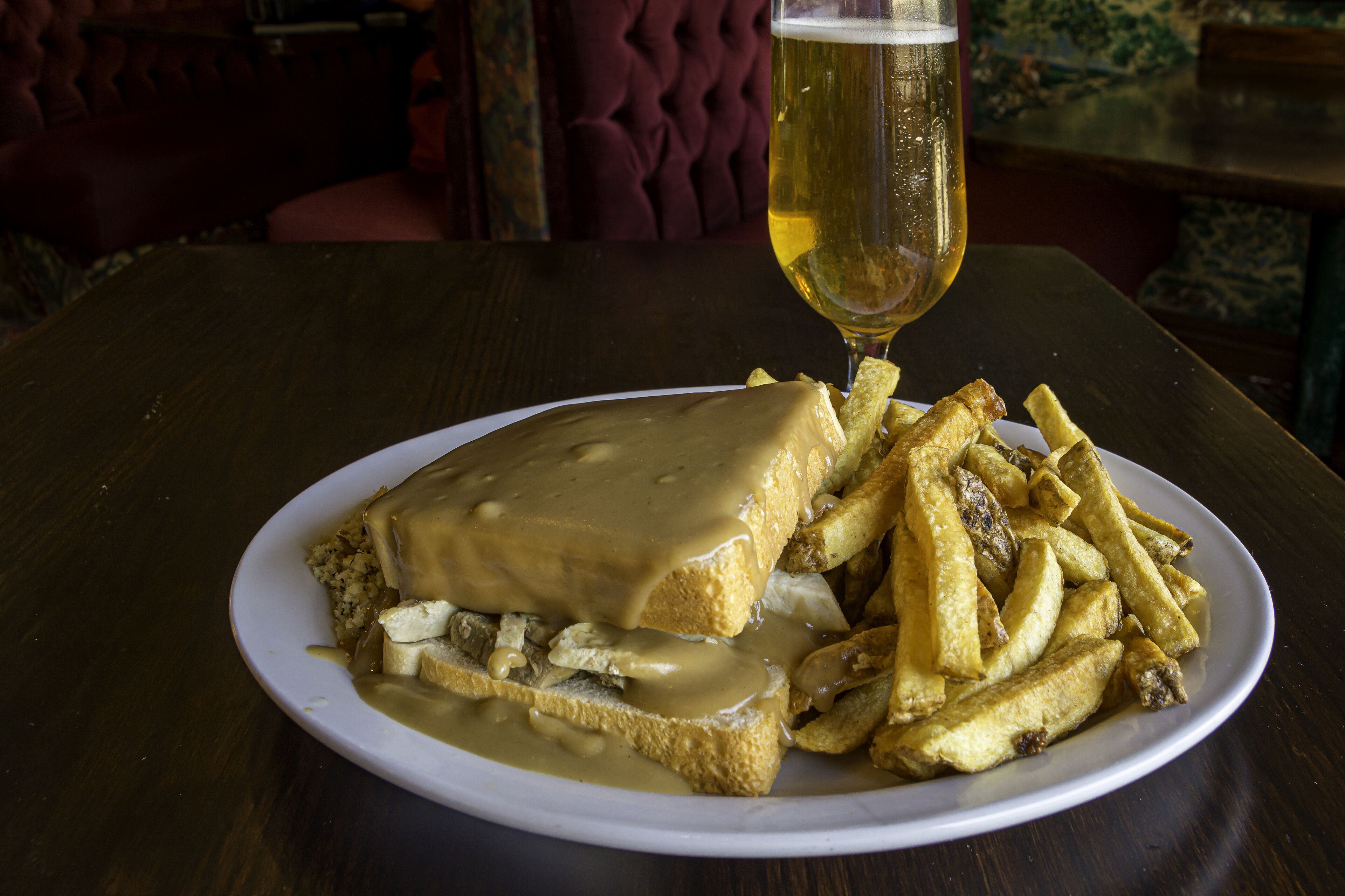 Un plato de comida con salsa y papas fritas, una jarra de cerveza y una mesa de madera oscura.
