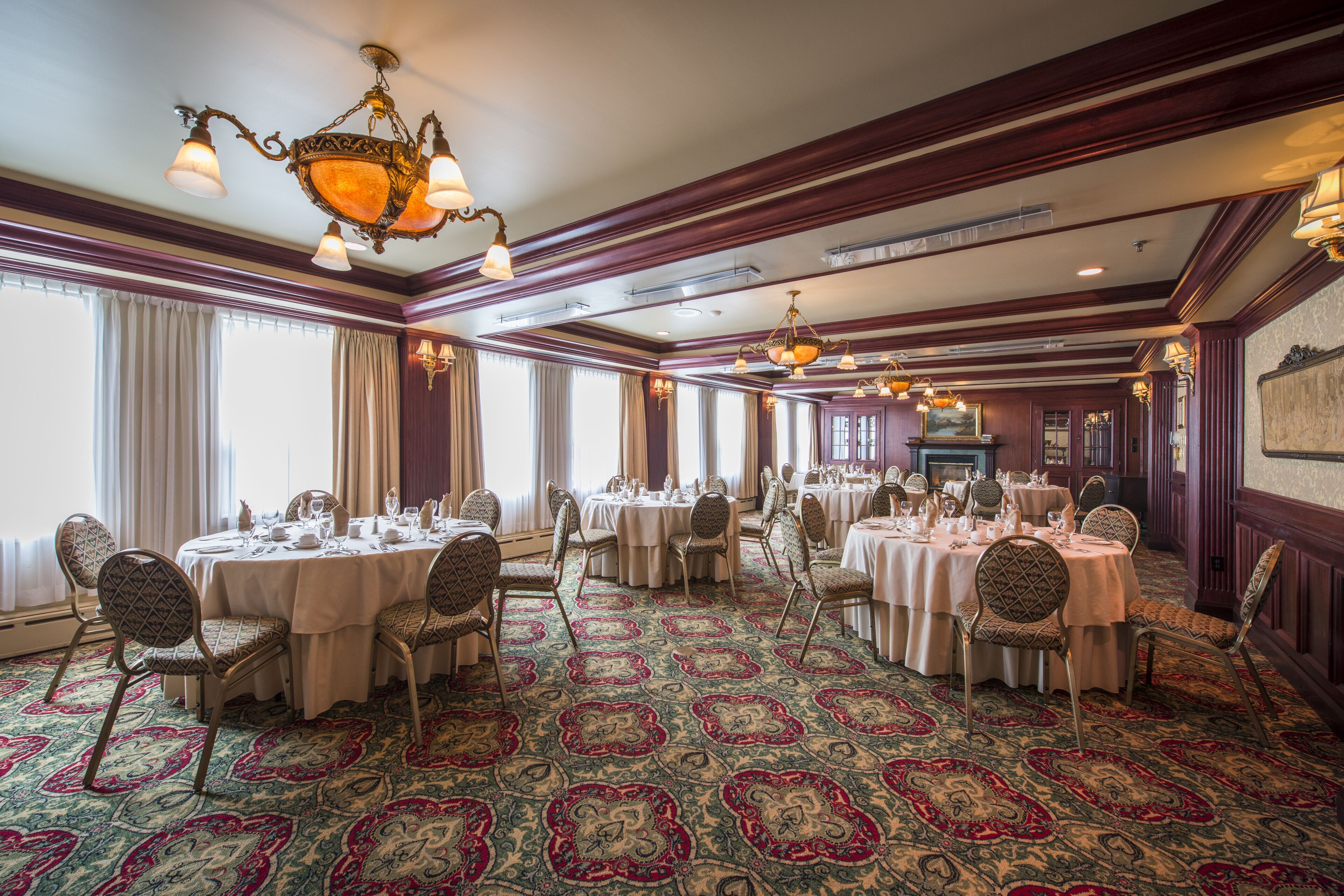 Un comedor formal con varias mesas redondas, sillas y candelabros ornamentados.