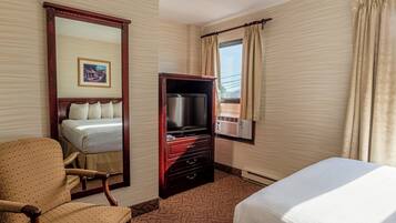 A hotel room with a bed, a television, a dresser, a chair, and a window with curtains.