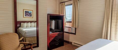 Una habitación de hotel con cama, televisión, cómoda, silla y ventana con cortinas.
