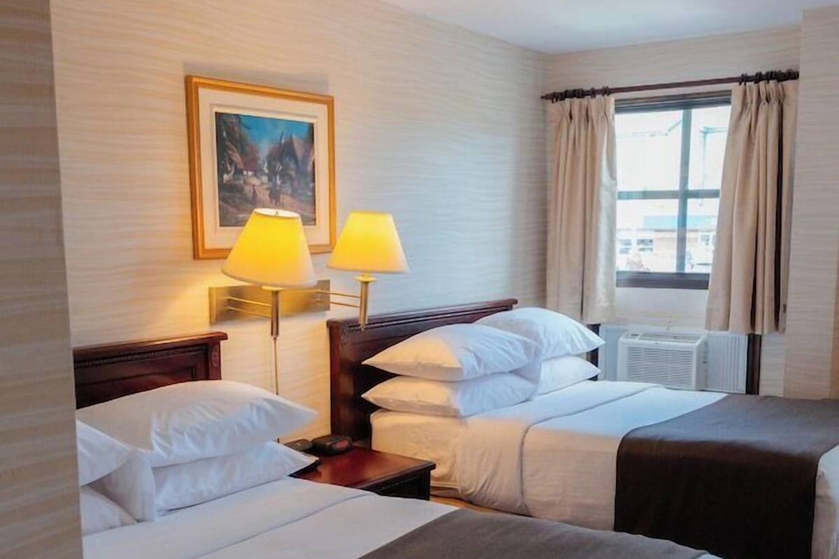 A hotel room with two beds, a window with curtains, a painting on the wall, and two bedside lamps.
