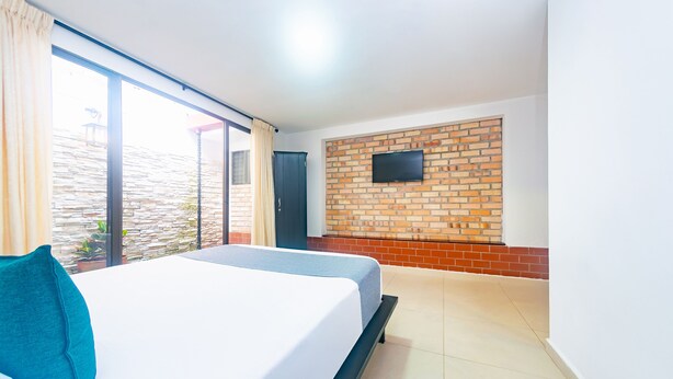 Une chambre d’hôtel avec un lit, un téléviseur fixé au mur en briques et une vue sur l’extérieur.