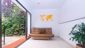 Une pièce avec un canapé marron, une carte du monde accrochée au mur, une plante en pot et une porte vitrée donnant sur un balcon agrémenté d’un mur végétal.