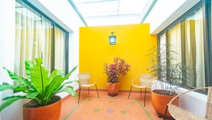 Une pièce lumineuse aux murs jaune vif, dotée d’un sol carrelé, de deux fauteuils en osier, d’une plante en pot et d’une lanterne fixée au mur.