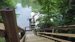 A wooden deck leading to a dock over a calm lake, surrounded by lush greenery.