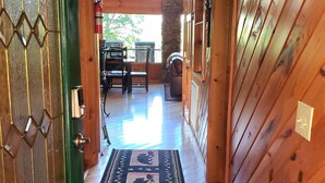 A wooden hallway with a patterned rug, a fire extinguisher, and a view of outdoor furniture.