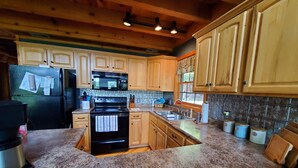 A kitchen with wooden cabinets, granite countertops, a black refrigerator, a microwave, and a stove.