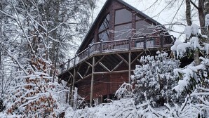 A wooden cabin with a balcony, surrounded by snow-covered trees.