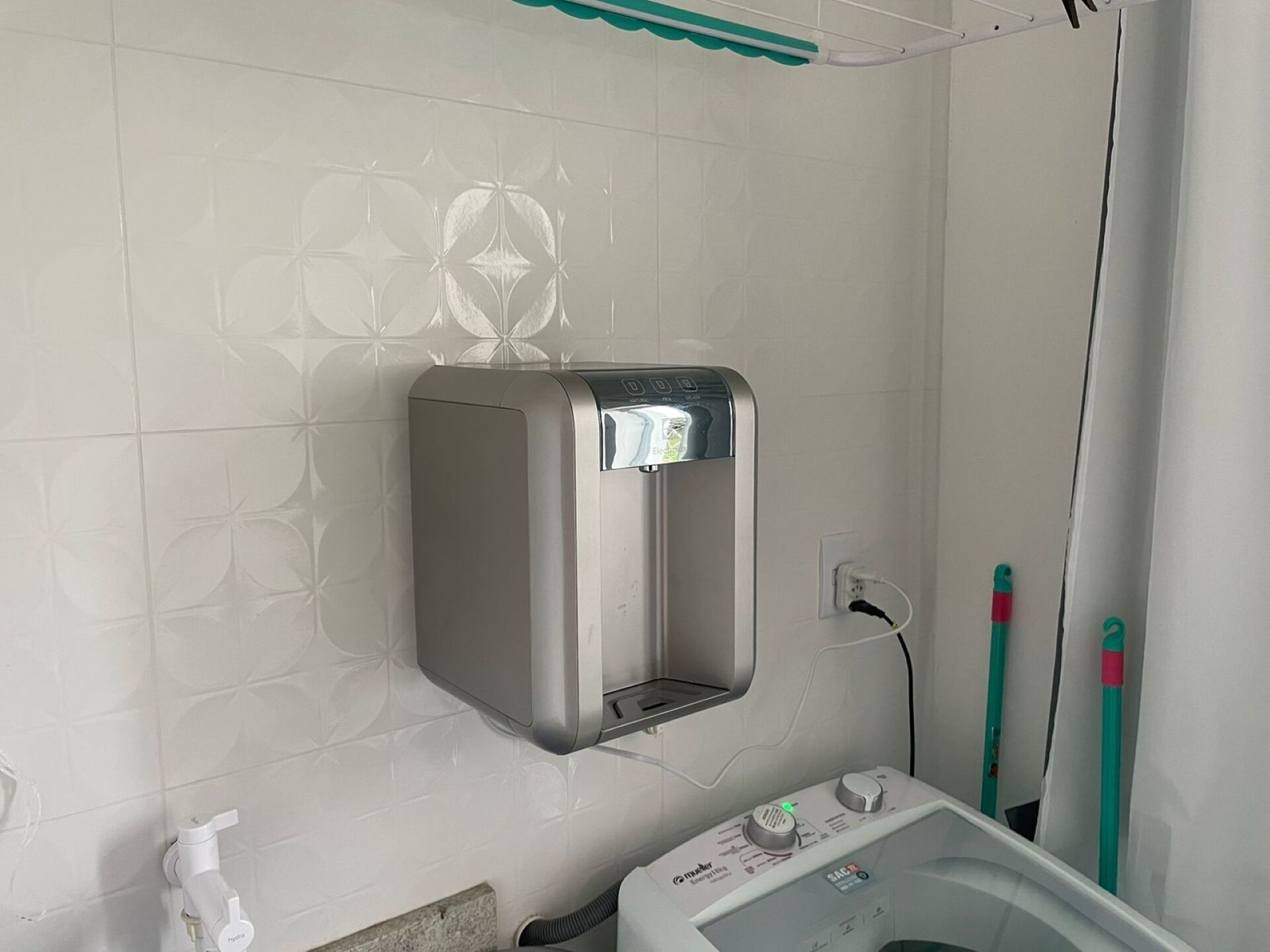 Een badkamer met een wandwaterdispenser, een handdroger en een prullenbak.