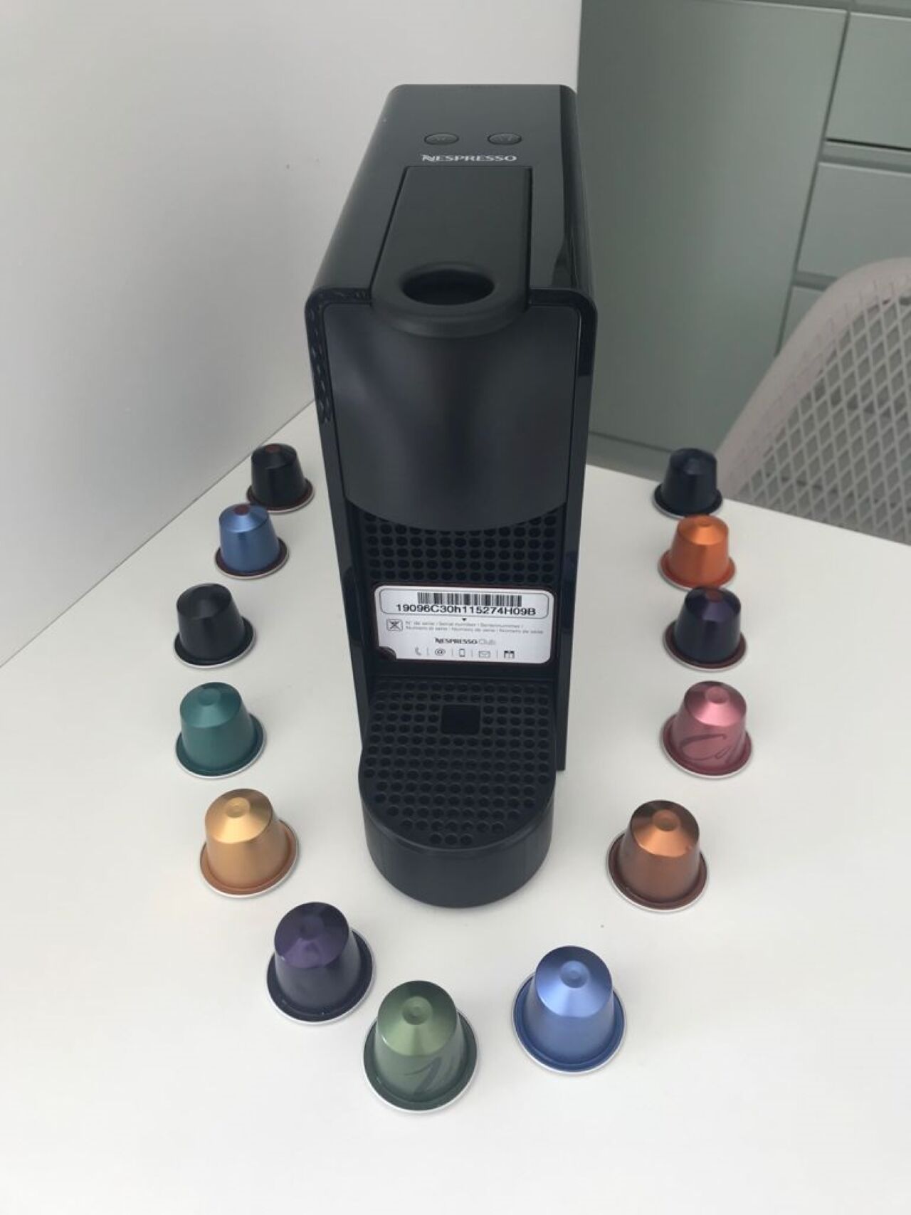 A black Nespresso machine with a barcode label, surrounded by various colored coffee capsules.