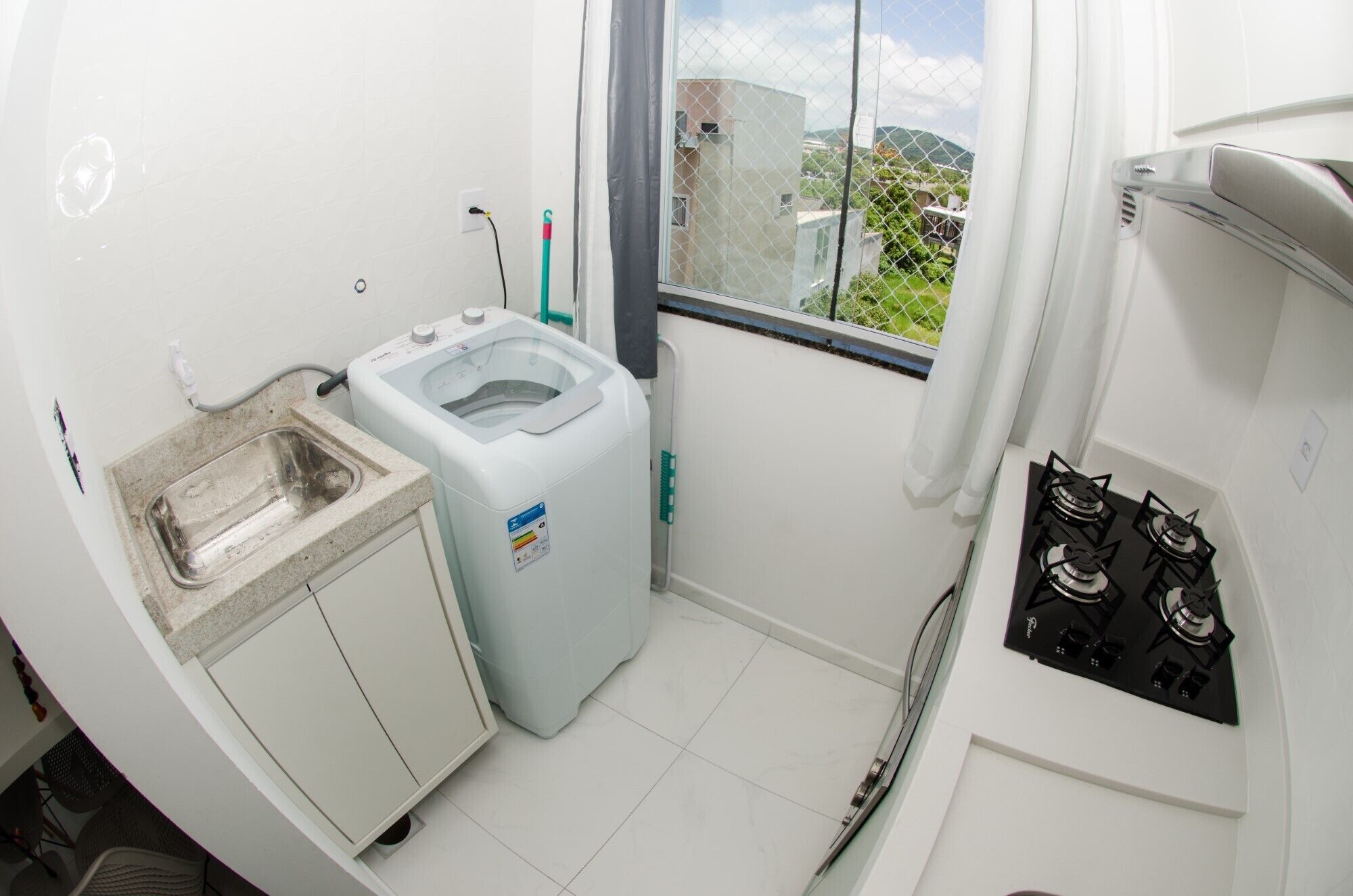 Une cuisine compacte équipée d’une cuisinière à gaz, d’un lave-linge et d’une fenêtre donnant sur des bâtiments et des espaces verts.