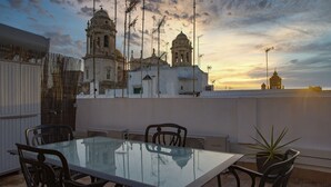 A rooftop terrace with a glass table and chairs, overlooking a historic building with bell towers.