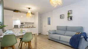 A modern kitchen with white cabinets, a dining area with green chairs, and a grey sofa.