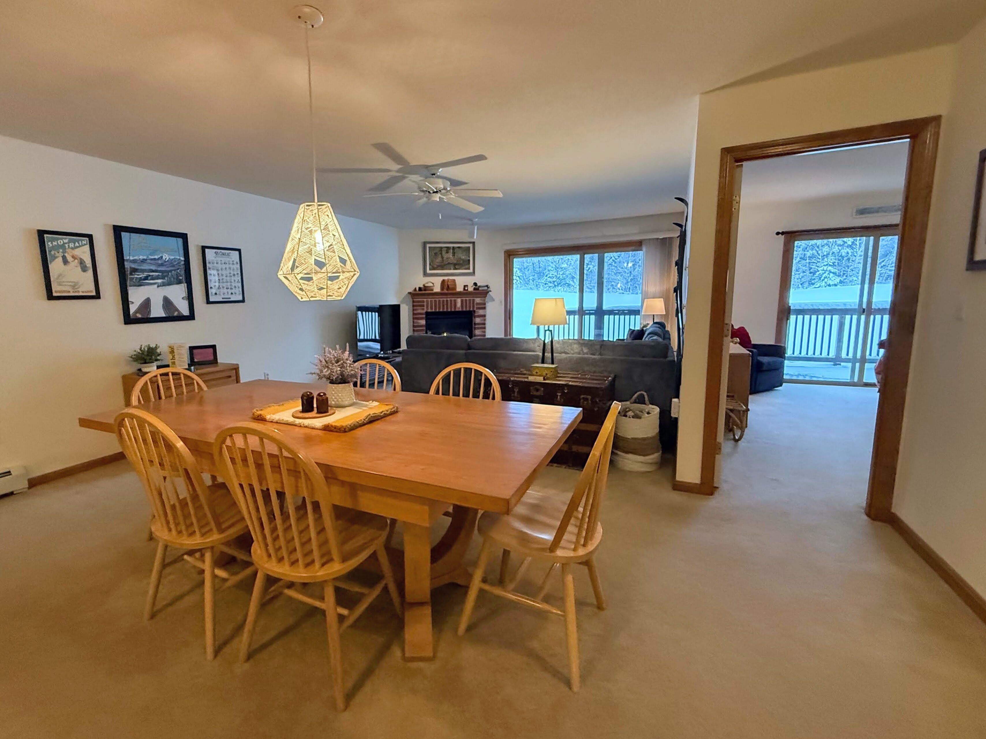 A dining area with a wooden table and chairs, a ceiling fan, and framed pictures on the wall.
