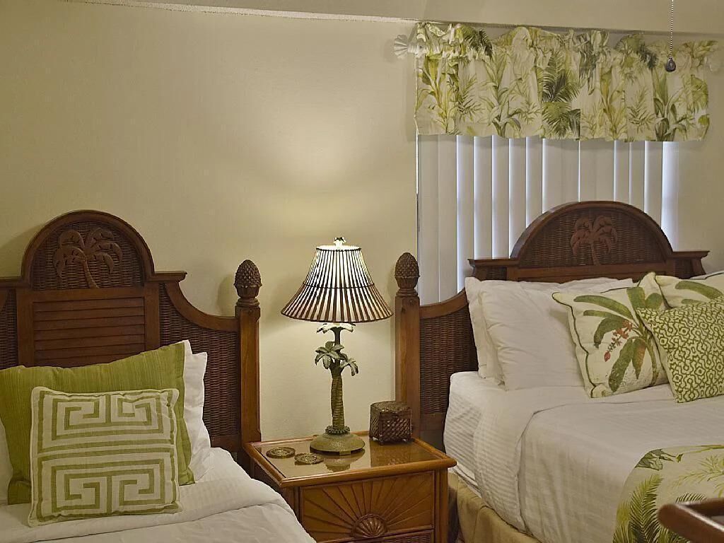 A hotel room with two beds, a nightstand with a lamp, and a window with a floral curtain.