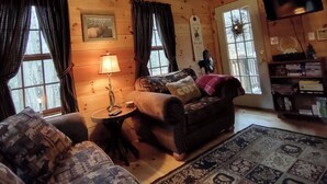 L’intérieur d’un chalet confortable, avec des murs en rondins, une tête de cerf fixée au plafond, une cheminée, un canapé et un tapis à motifs.