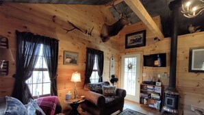 L’intérieur d’un chalet accueillant, avec un canapé, un tapis, une lampe, une cheminée et un téléviseur.