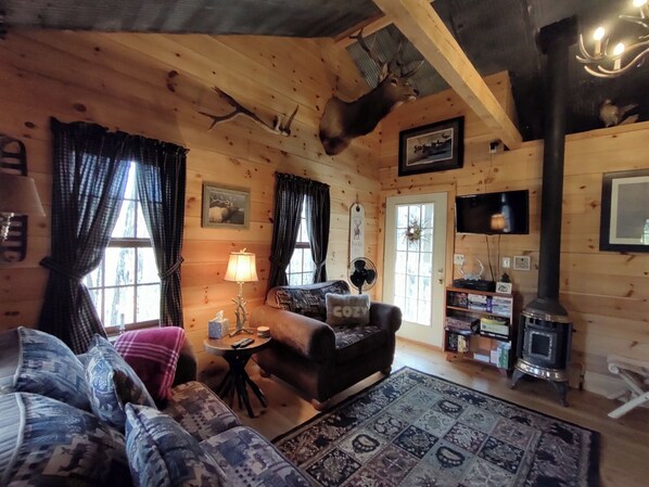 Un interior de cabaña acogedor con sofá, alfombra, lámpara, chimenea y televisor.