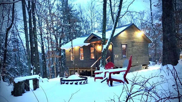 Une cabane aux murs en bois, entourée d’arbres couverts de neige.
