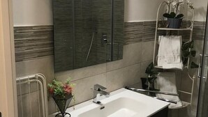 Ein modernes Badezimmer mit einem großen Spiegel, einem weißen Waschbecken und einer Duschkabine aus Glas.