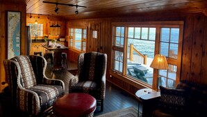 A cozy cabin interior with wooden walls, a dining area, and large windows overlooking a body of water.