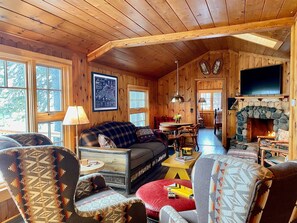 A cozy log cabin interior with a living room, dining area, and stone fireplace.