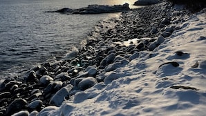 A snowy beach with a rocky shoreline and a view of the ocean under a partly cloudy sky.