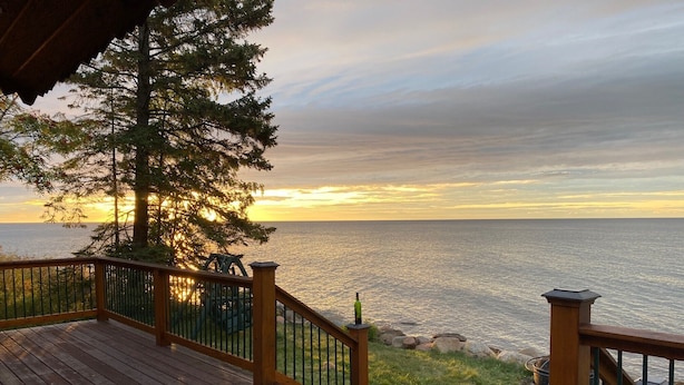 A wooden deck with a railing overlooking a body of water during sunset.