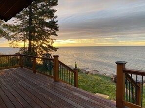 A wooden deck with a railing overlooking a body of water during sunset.